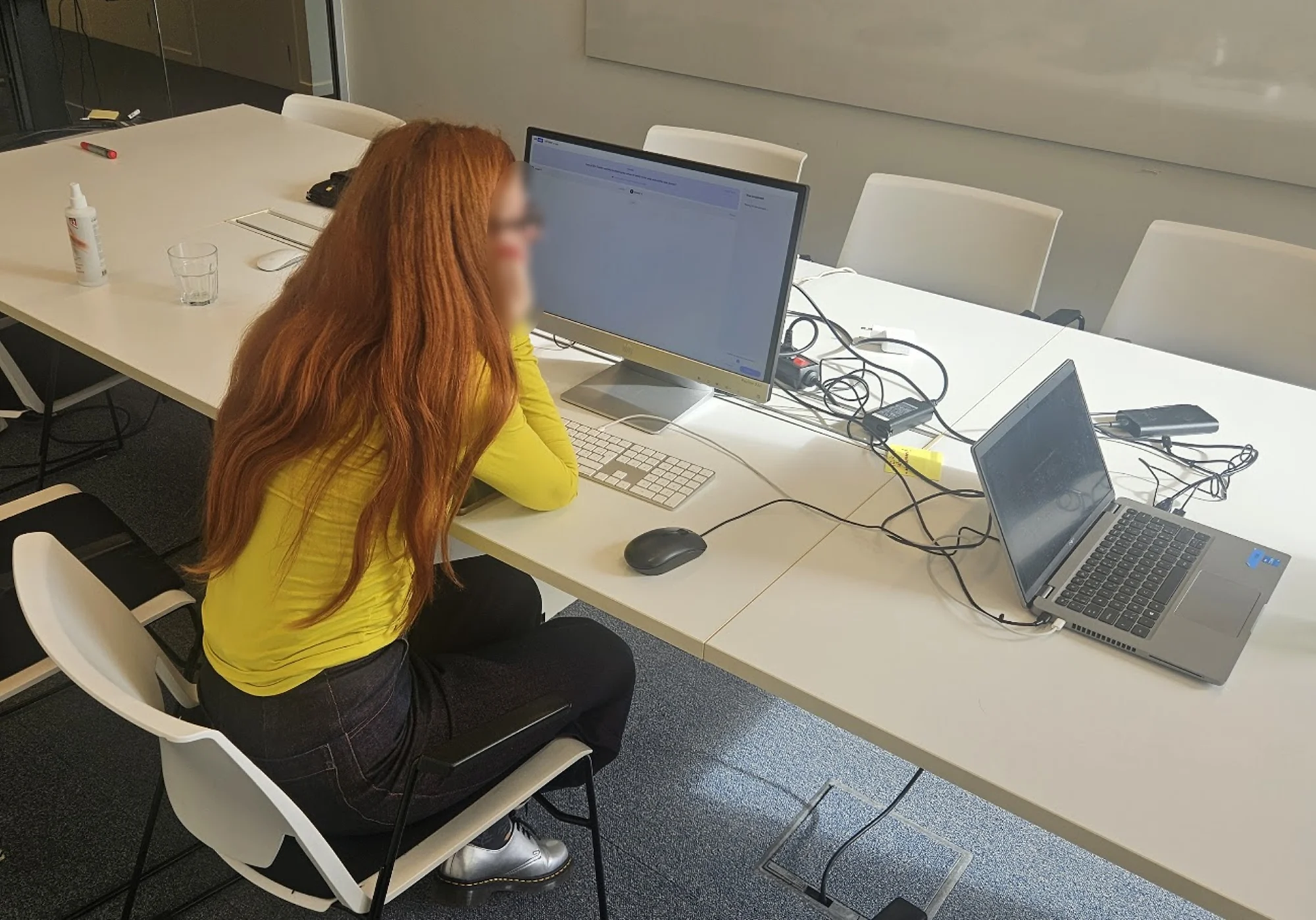 A participant at a desk during the trial, comparing two agents on a monitor while the session runs on a laptop beside her.